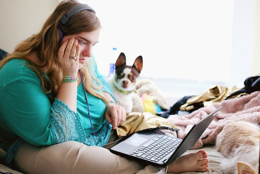 woman with autism sits on bend looking at laptop, concerned, she has a small dog on bed with her