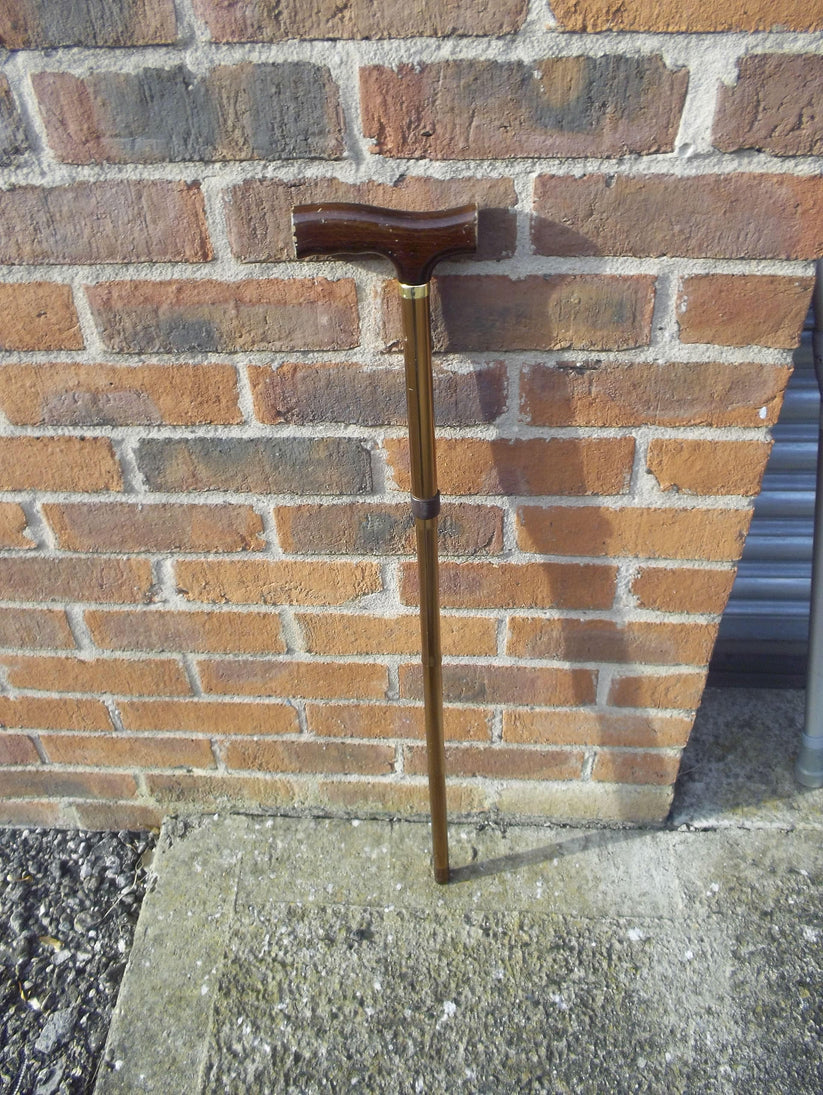 dark wooden handle with bronze walking stick agains a brickwall background